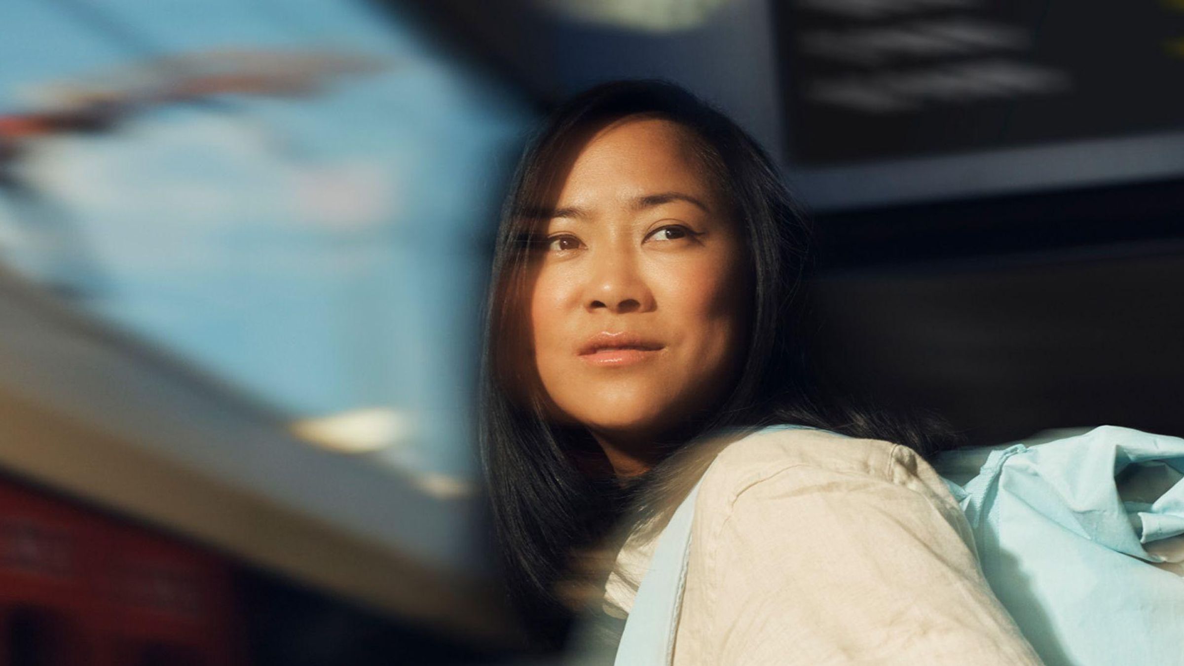 A woman wearing a yellow shirt and blue backpack gazes into the distance with a dreamy expression.